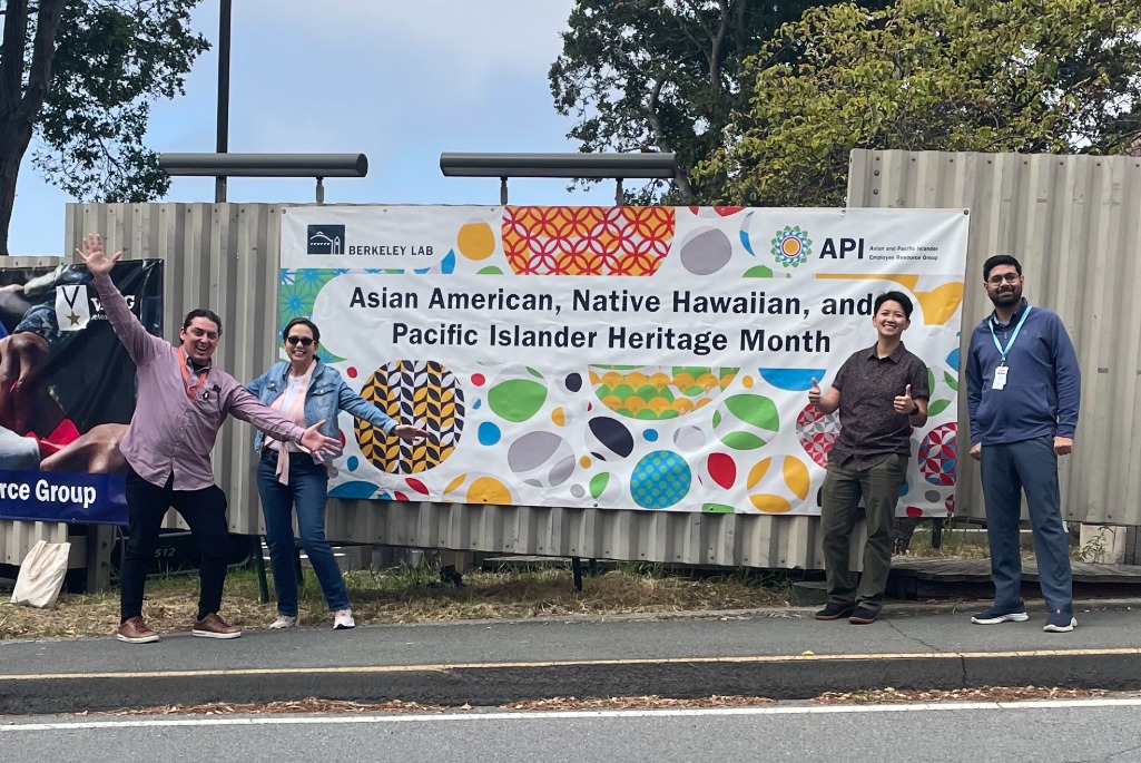 Four persons standing in front of large mounted banner reading "Asian American, Native Hawaiian, and Pacific Islander Heritage Month"