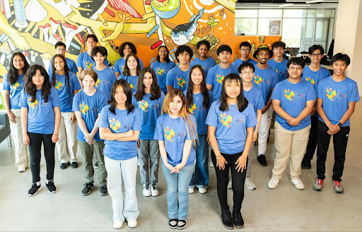 a group of about 25 students in blue T-shirts standing in front of a mural