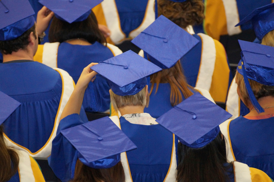 Rear view close-up of persons wearing blue graduation hats and blue and gold robes