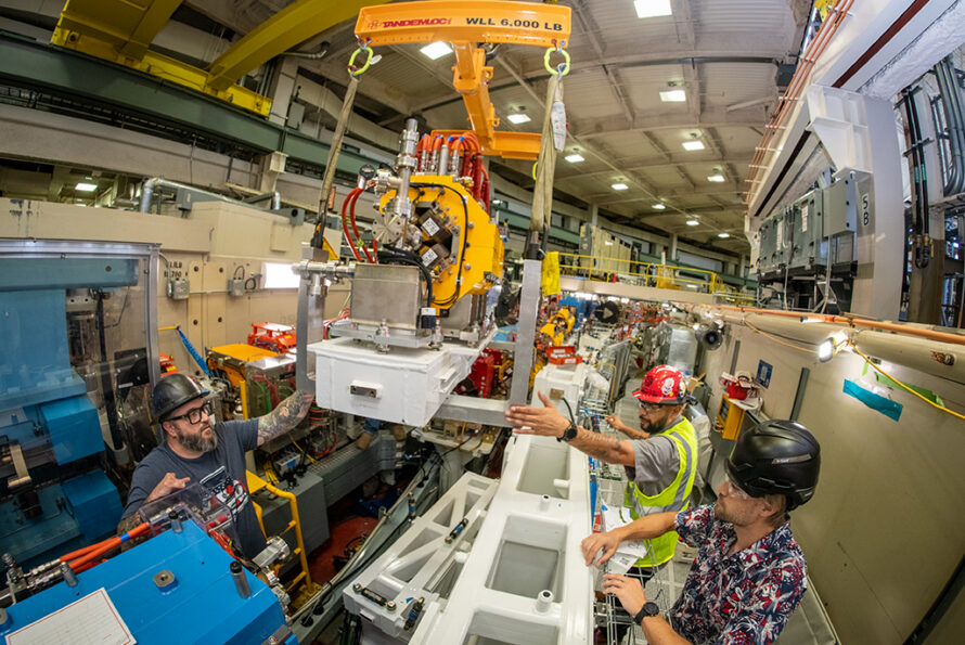 People in safety gear moving a large piece of scientific equipment.