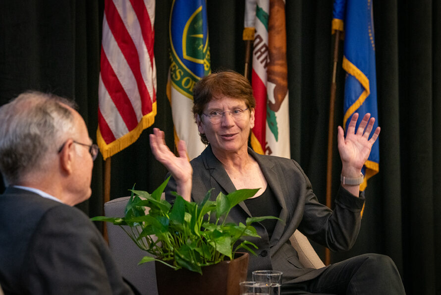 Two persons sitting on a stage looking at each other with one person with their arms in the air.