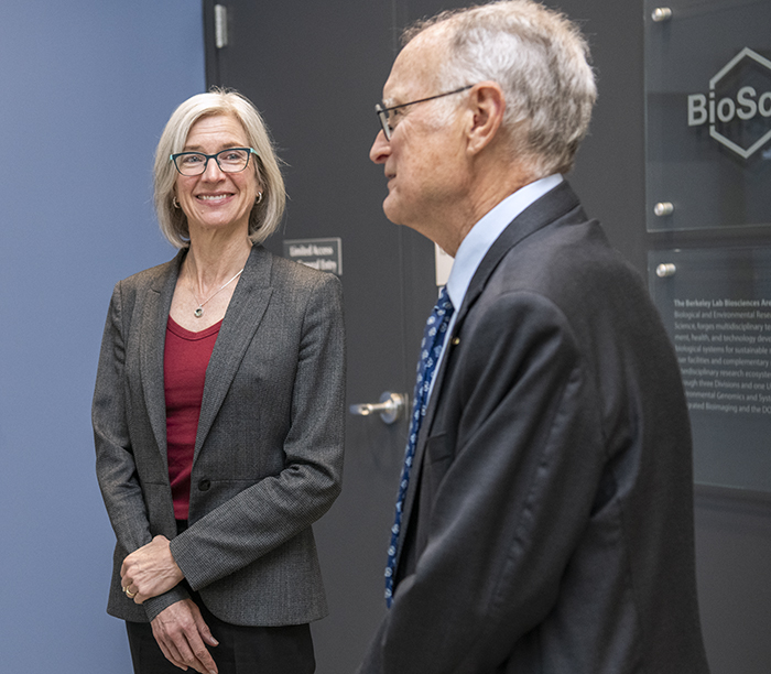 Two persons standing in front of supercomputer both wearing glasses and dark suit jackets.