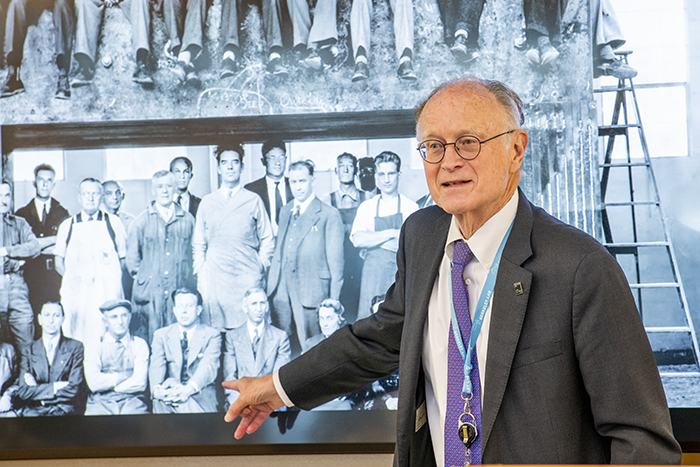 Person in dark suit jacket and purple tie standing in front of old black and white photo.