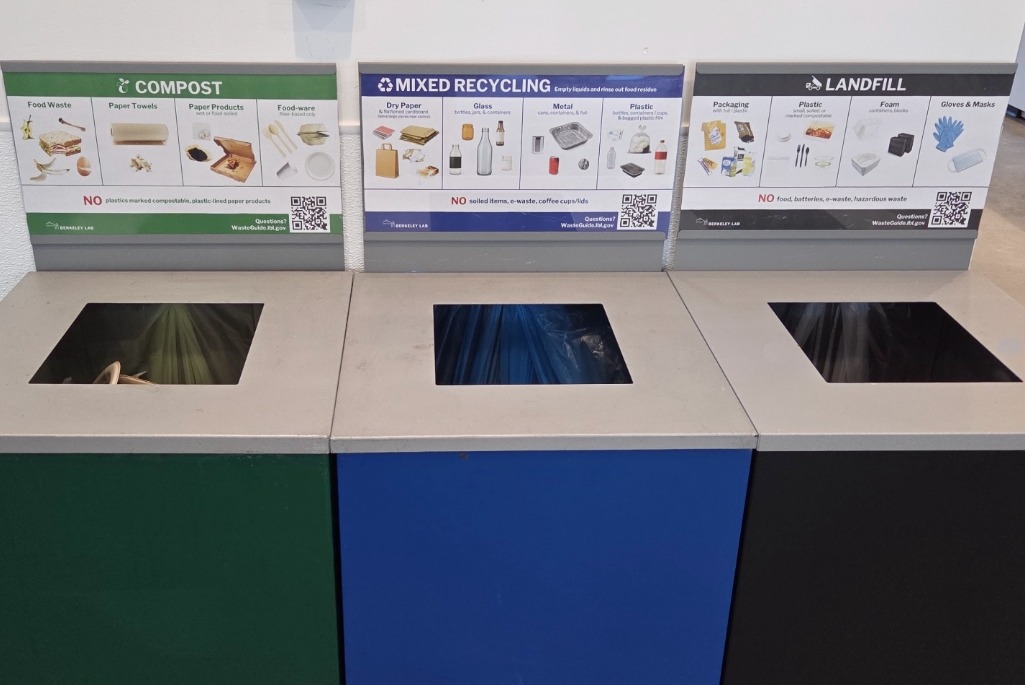 Three recycle bins adjacent to one another: a green bin is labeled "Compost"; a blue bin is labeled "Mixed Recycle"; and a black one is labeled "Landfill"