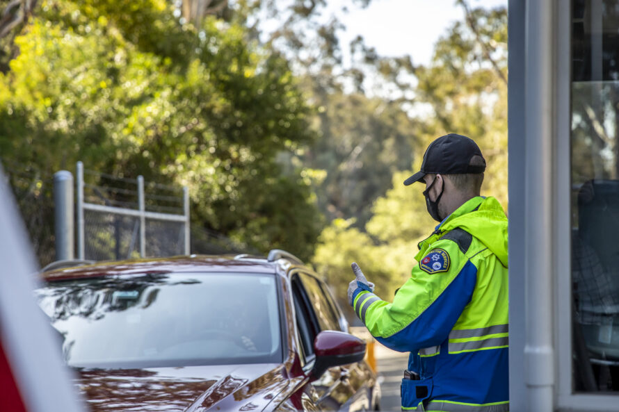 Car beside Berkeley Lab gateway entrance with gate guard in neon yellow jacket approaching vehicle