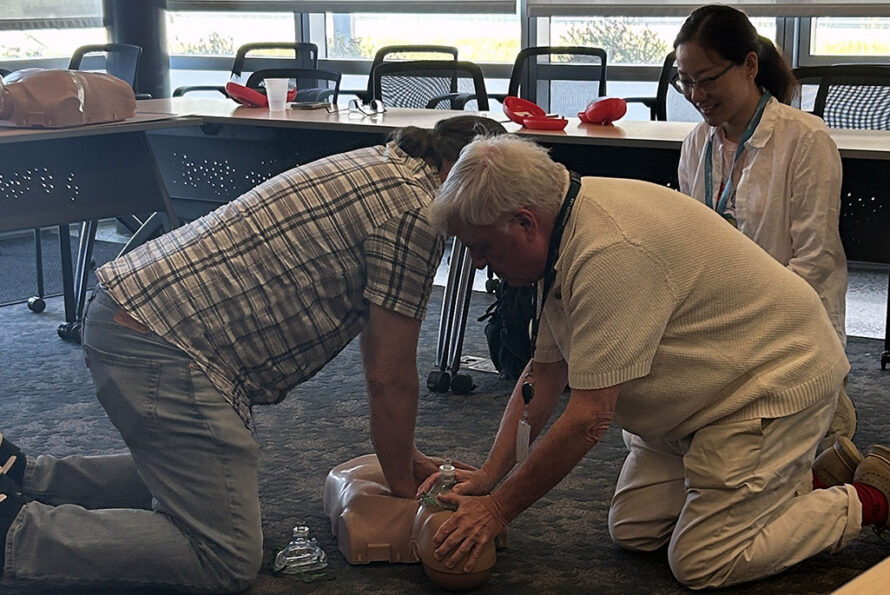 Two people performing CPR on a manikin with a third person observing.