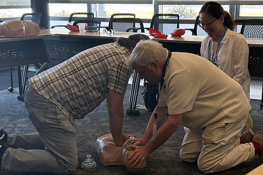Two people performing CPR on a manikin with a third person observing.