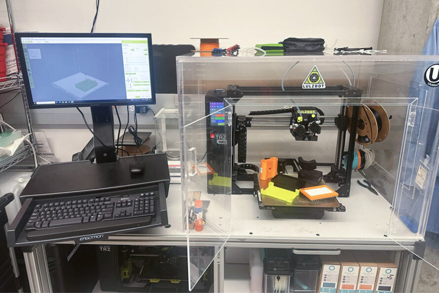 A desk with a 3D printer next to a computer.