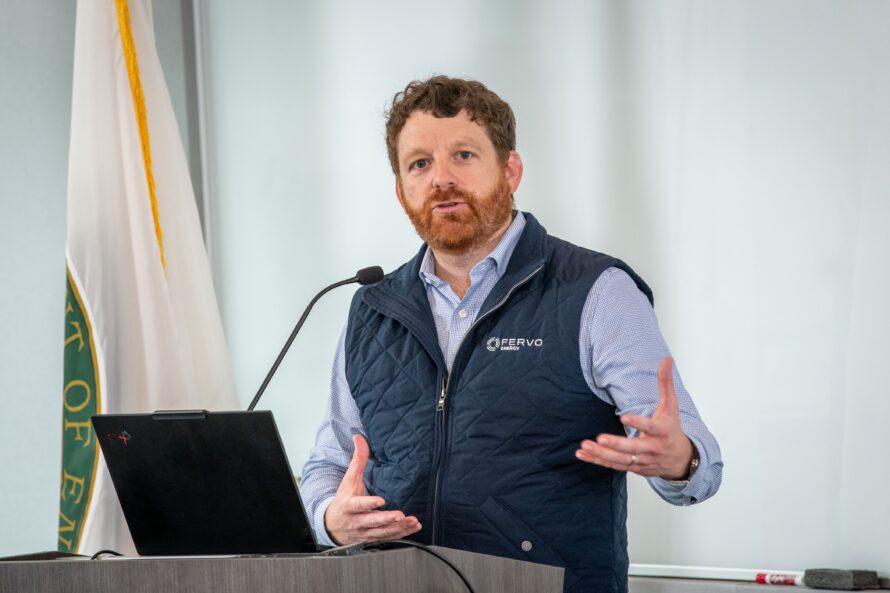 Tim Latimer, CEO of Fervo Energy, a person with auburn hair and beard wearing a light blue dress shirt under a dark blue vest speaking at a podium.