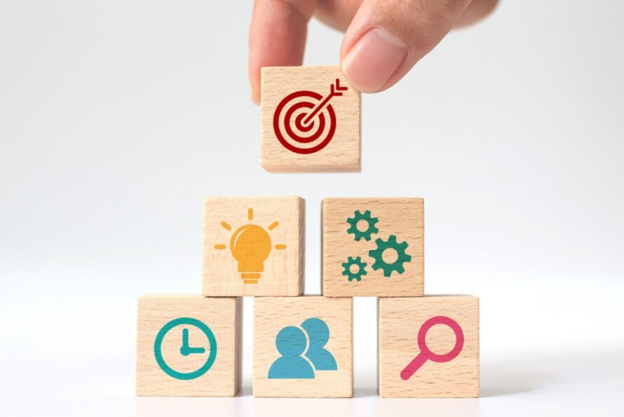 A hand stacking blocks with different icons representing goals and priorities.