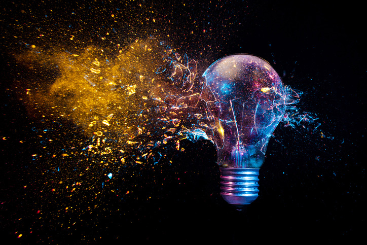 explosion of a traditional electric bulb. shot taken in high speed, at the exact moment of impact. Colored lights and black background. concept of creativity and fragility.