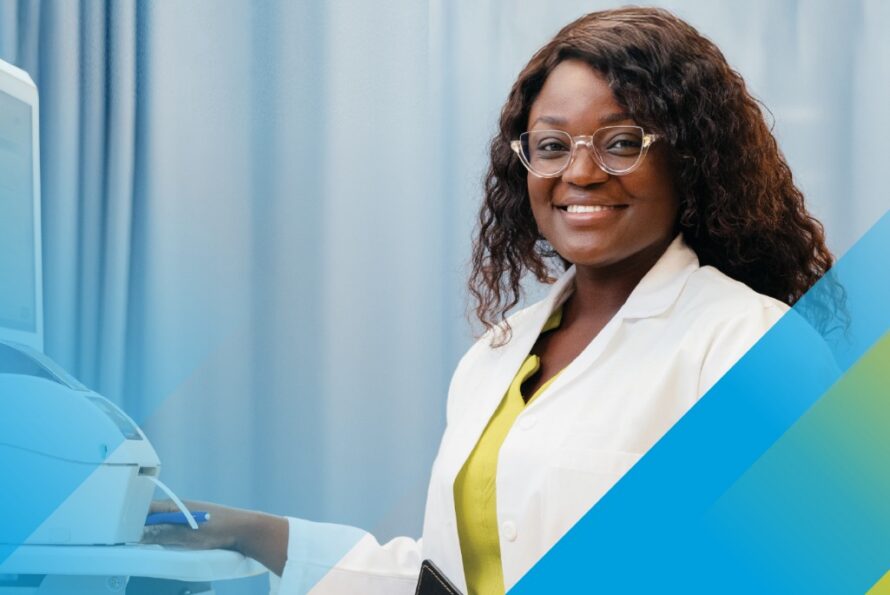A woman in a lab coat stands next to a computer